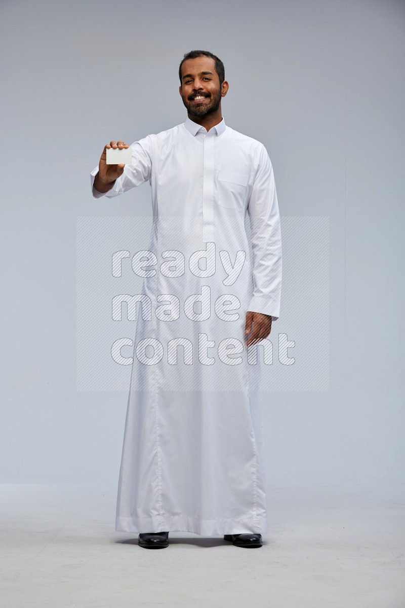 Saudi man wearing Thob standing holding ATM card on Gray background