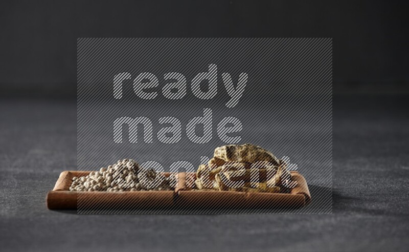 مربعان من أعواد القرفة ممتلئان بحبوب الفلفل الأبيض وأصابع الكركم علي خلفية سوداء