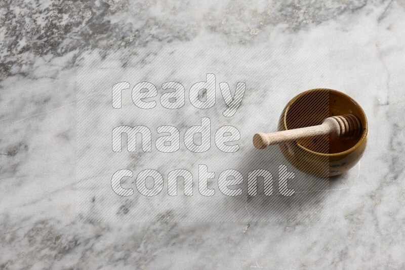 Multicolored pottery bowl with wooden honey dipper in it on grey marble background