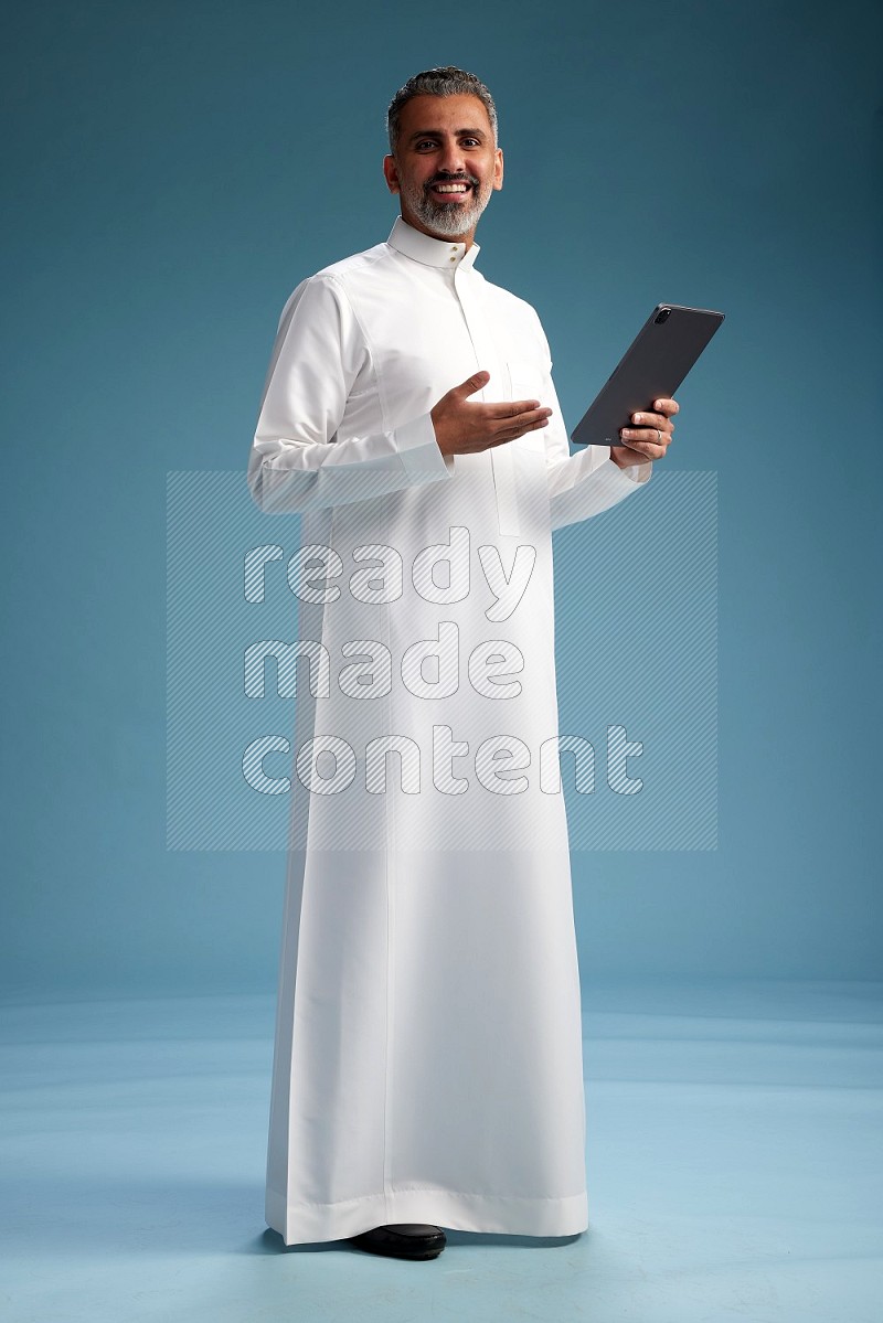 Saudi man waring thob with tablet on blue background