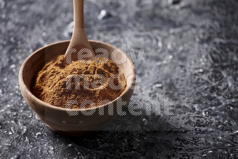 Wooden bowl full of cinnamon powder with a wooden spoon on a textured black background in different angles