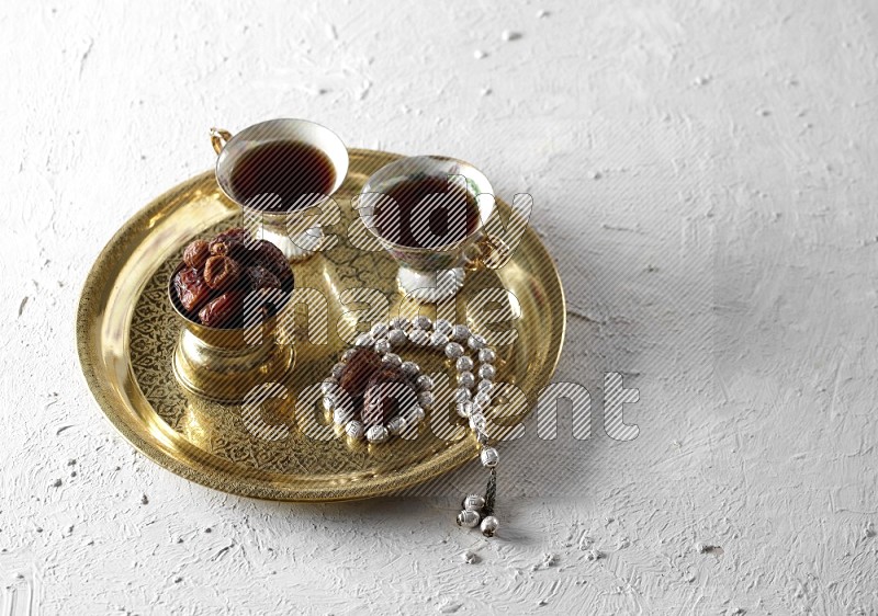 تمر في وعاء معدني مع شاي وسبحة على صينية معدنية علي خلفية بيضاء