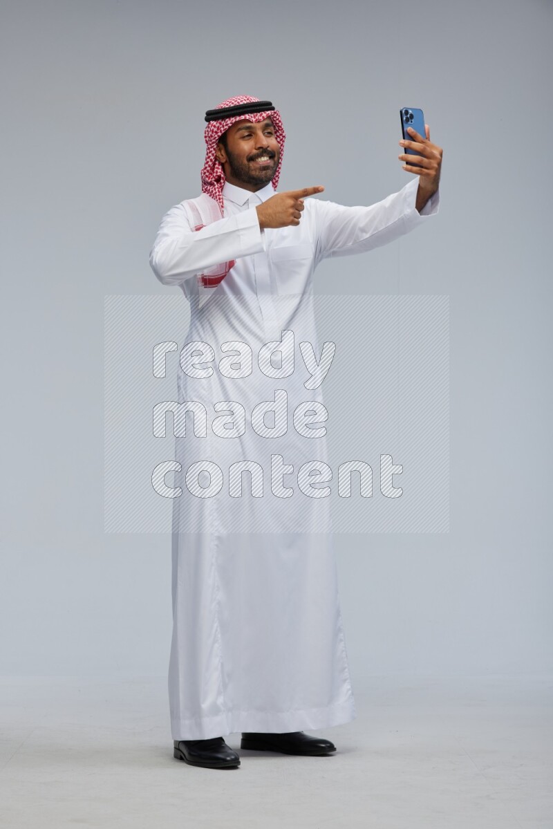 Saudi man Wearing Thob and shomag standing taking selfie on Gray background