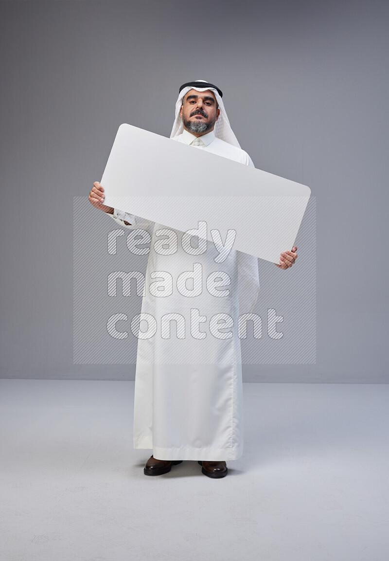 Saudi man Wearing Thob and white Shomag standing holding board on Gray background