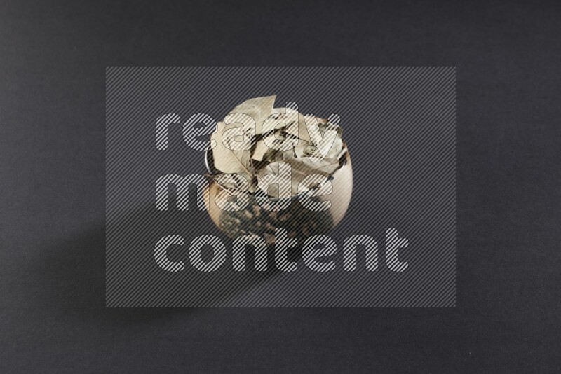 A multicolored pottery bowl full of dried bay leaves on black flooring