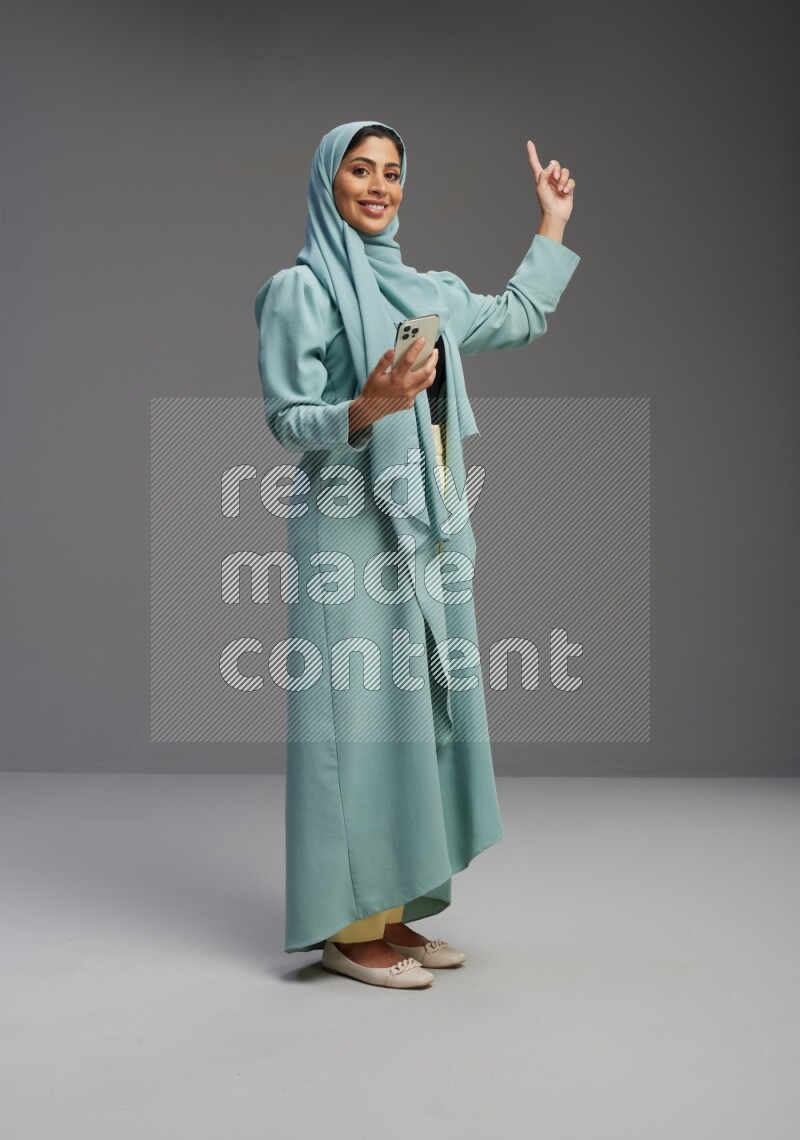 Saudi Woman wearing Abaya standing texting on phone on Gray background
