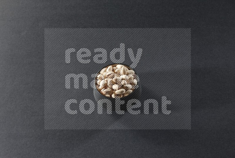 A black pottery bowl full of pistachios on a black background in different angles