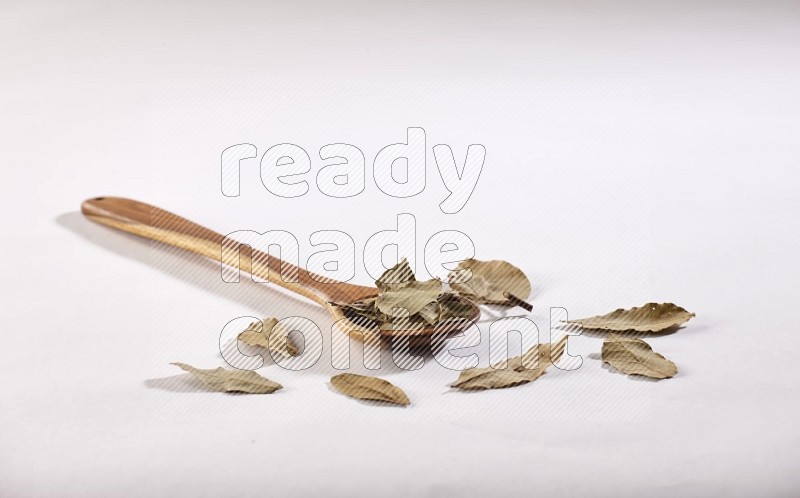 A wooden ladle filled with dried bay leaves on white flooring in different angles