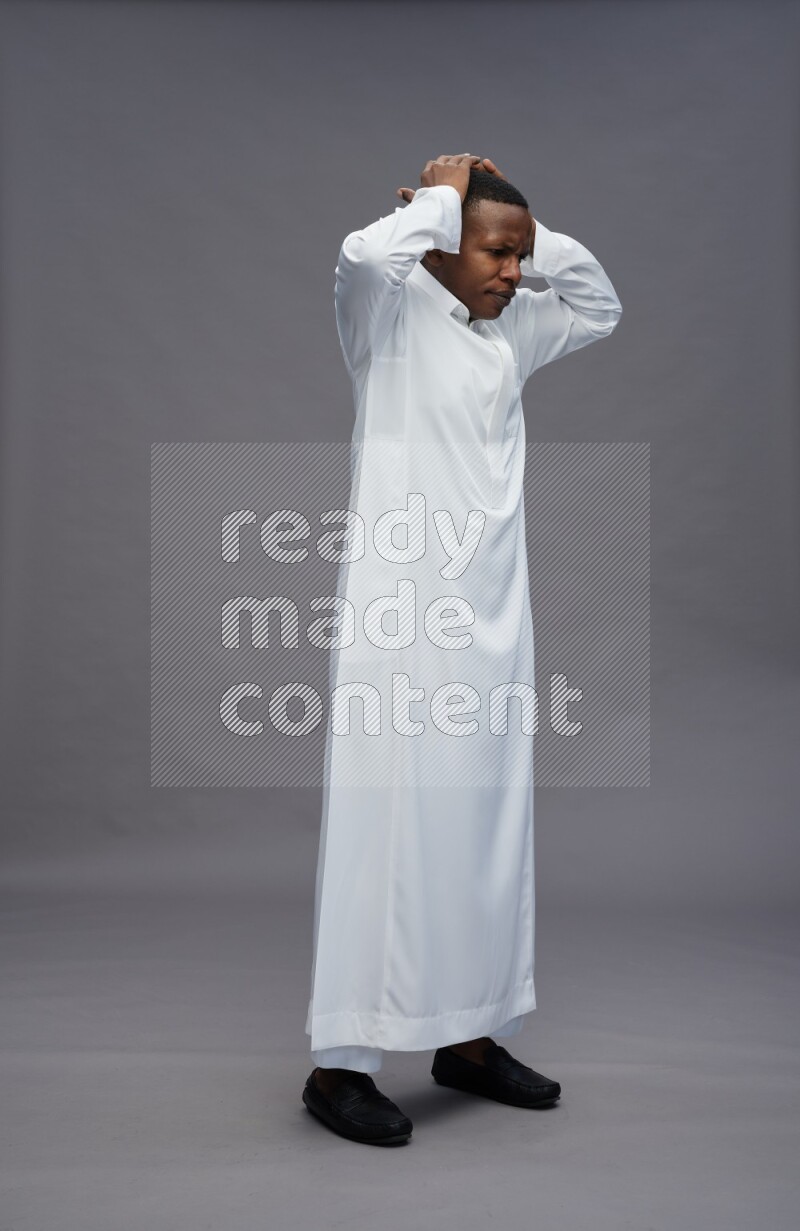 Saudi man wearing thob standing hands behind head on gray background