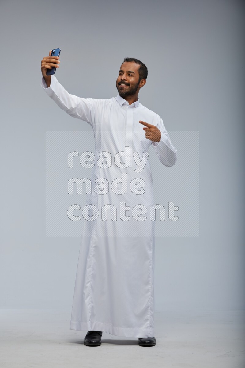 Saudi man wearing Thob standing taking selfie on Gray background