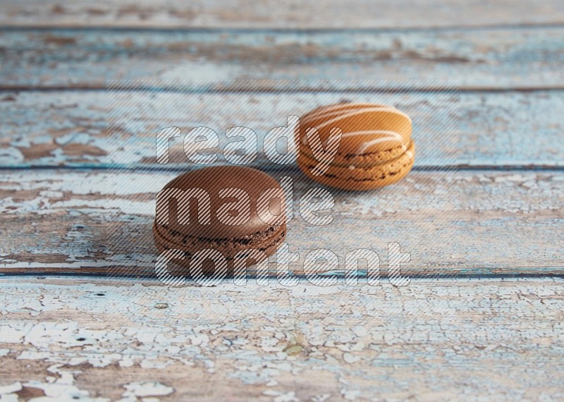 45º Shot of of two assorted Brown Irish Cream, and Brown Dark Chocolate macarons on light blue background