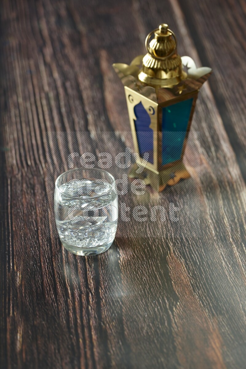 A golden lantern with different drinks, dates, nuts, prayer beads and quran on brown wooden background