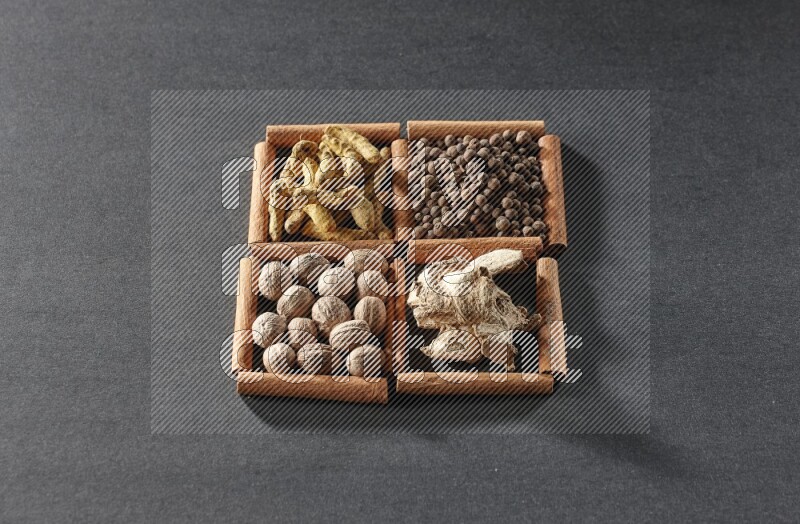 4 مربعات من عيدان القرفة ممتلئة بأصابع الكركم وبهار الفلفل الحلو والزنجبيل المجفف وجوزة الطيب على أرضية سوداء