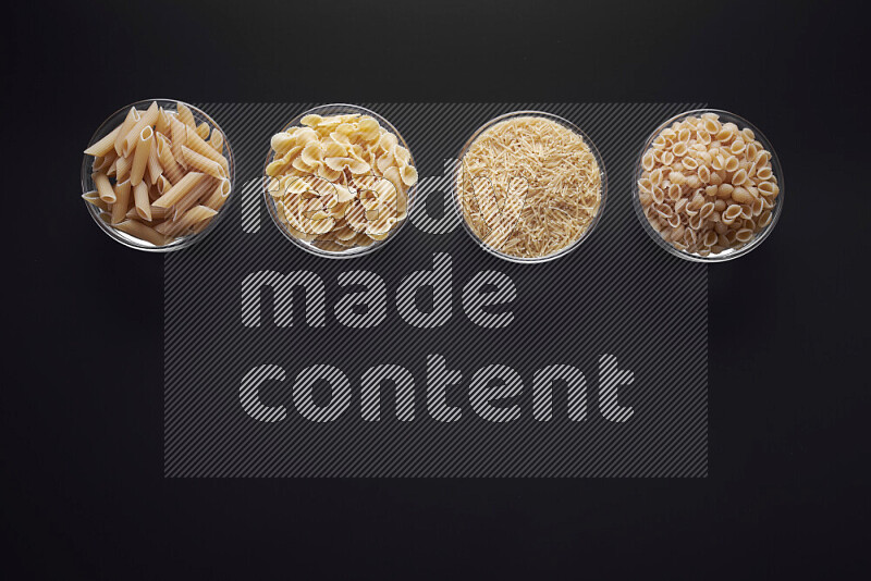 Different pasta types in glass bowls on black background