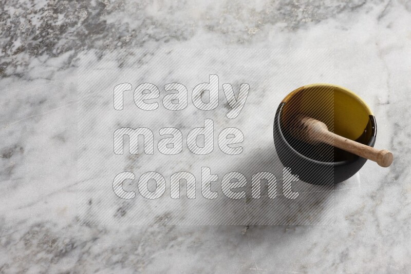 Multicolored pottery bowl with wooden honey dipper in it on grey marble background