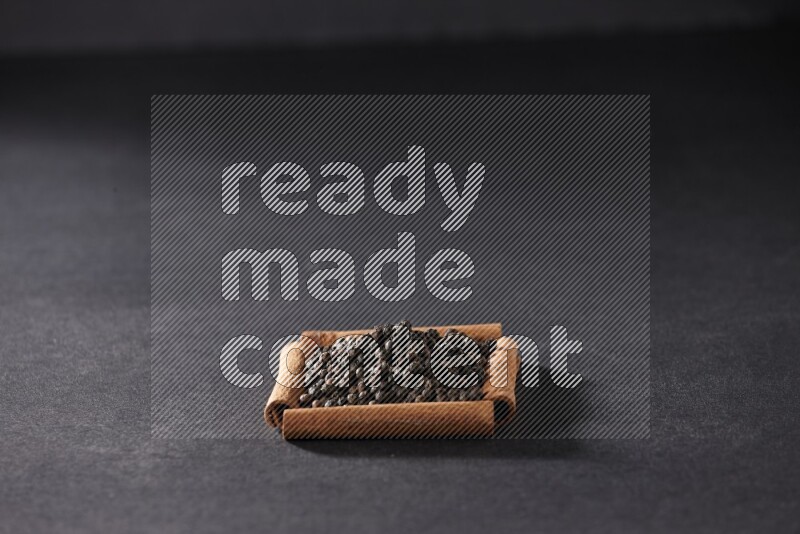 A single square of cinnamon sticks full of black pepper on black flooring