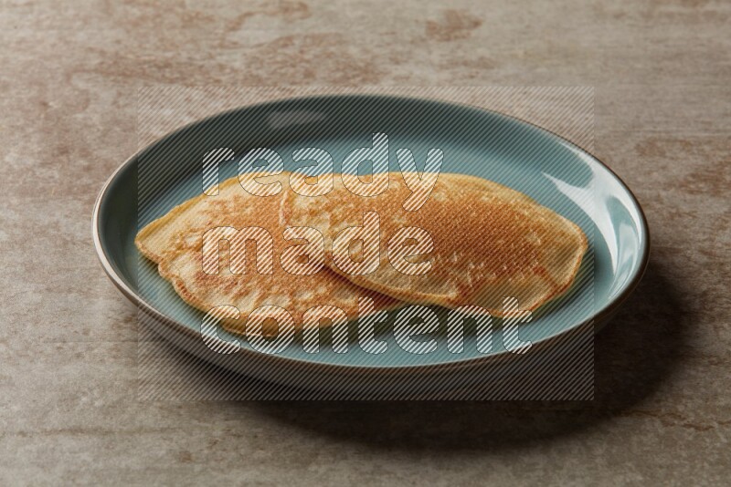Two stacked plain pancakes in a blue plate on beige background