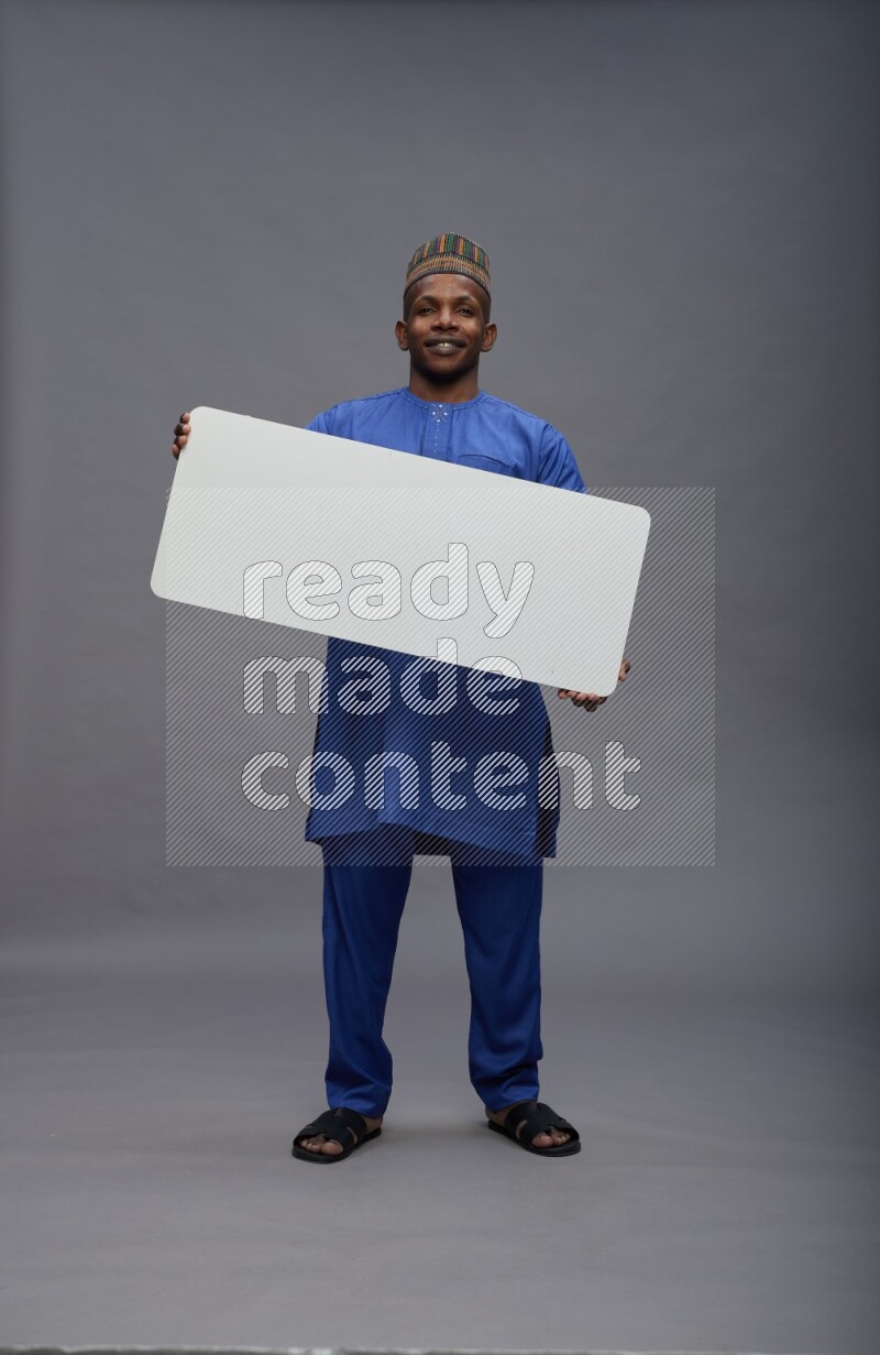 Man wearing Nigerian outfit standing holding board on gray background