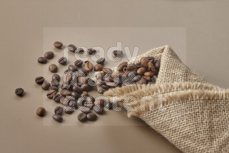 Spilled roasted coffee beans from its pack on beige background