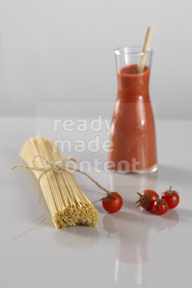 Raw pasta with tomatoe pasta with different ingredients such as cherry tomatoes, basil, garlic, bay laurel, cardamom, white pepper, black pepper, red chilis and wheat stalks on light grey background