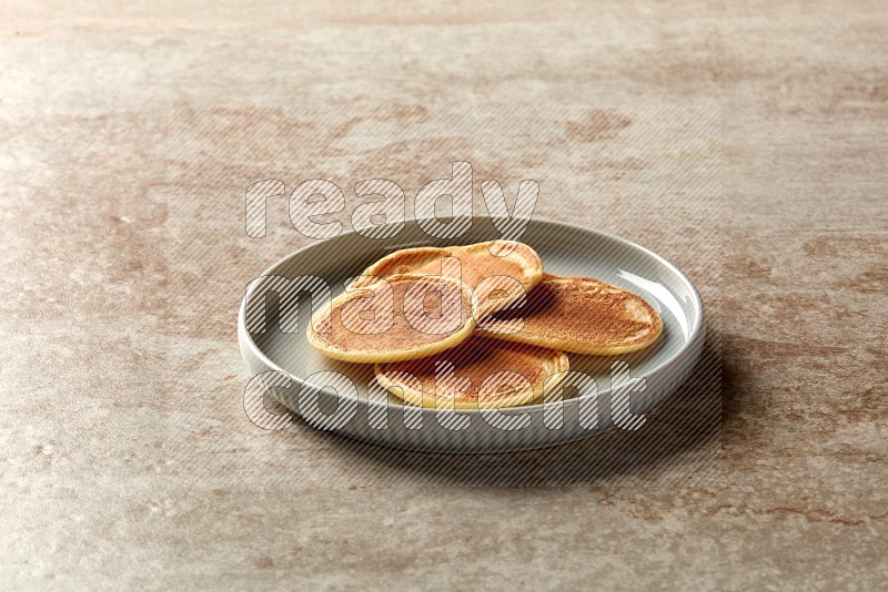 Four stacked plain mini pancakes in a blue plate on beige background