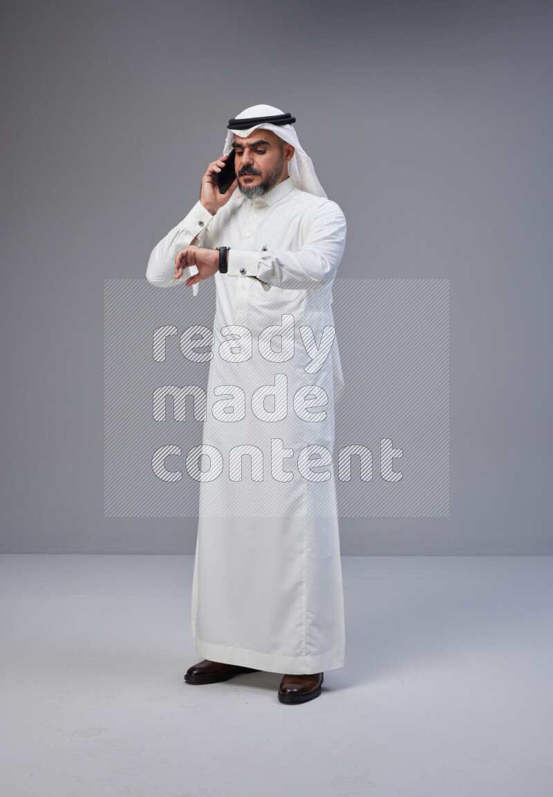 Saudi man Wearing Thob and white Shomag standing talking on phone on Gray background