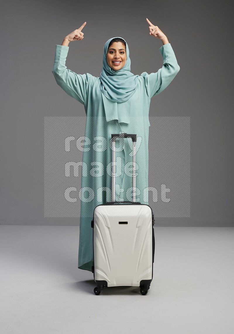 Saudi Woman wearing Abaya standing holding Travel bag on Gray background