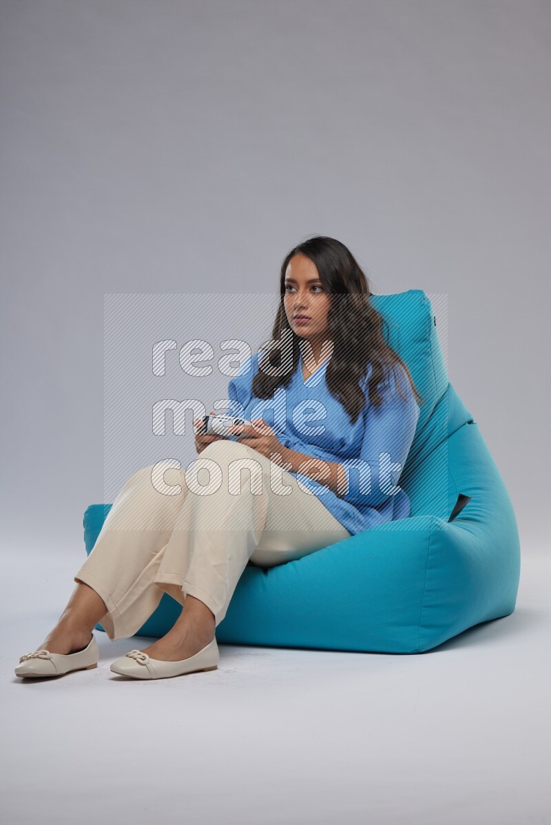 A woman sitting on a blue beanbag and gaming with joystick