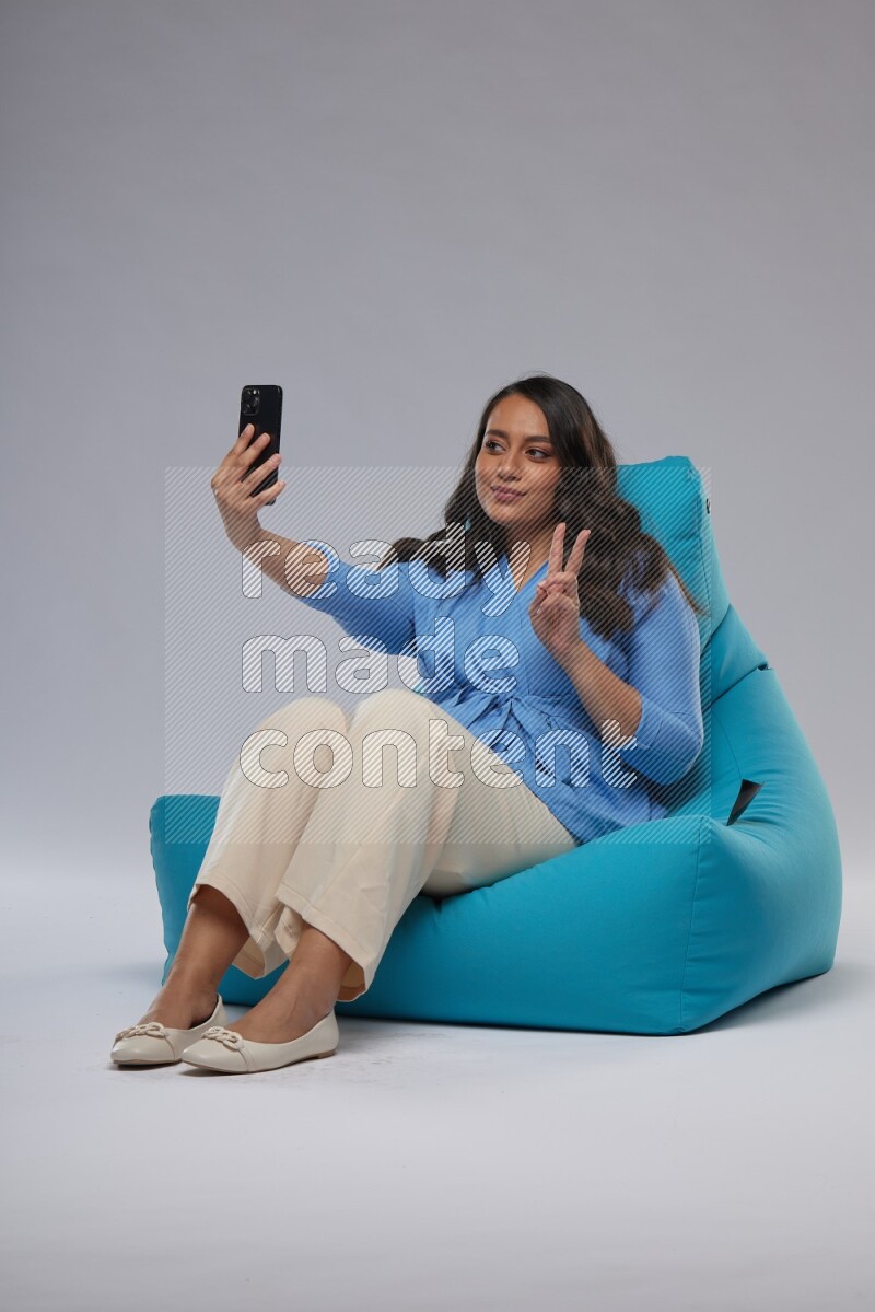 A woman sitting on a blue beanbag and taking selfie