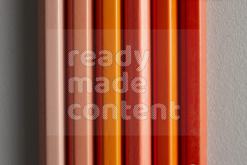 مجموعة من أقلام الرصاص الملونة مرتبة لتعرض تدرجا من الألوان البرتقالية علي خلفية رمادية