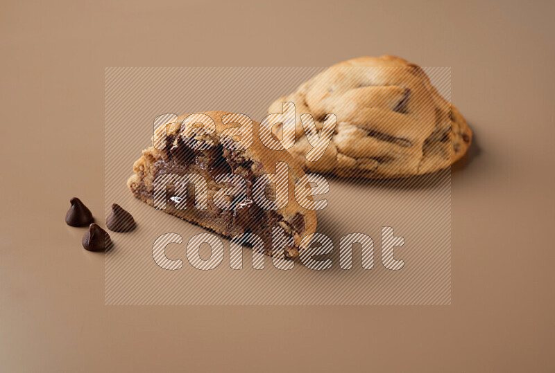 a chocolate chip cookie with another one cut in half on a brown background