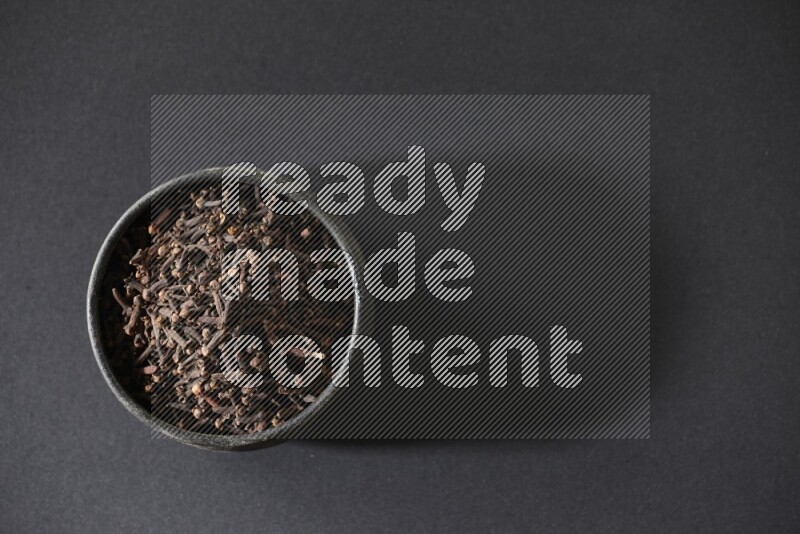 A black pottery bowl full of cloves on a black flooring