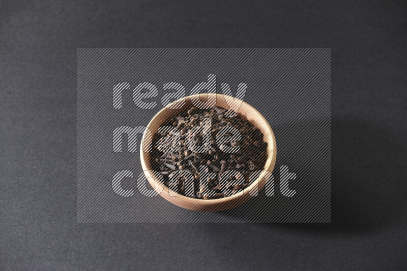A wooden bowl full of cloves on a black flooring