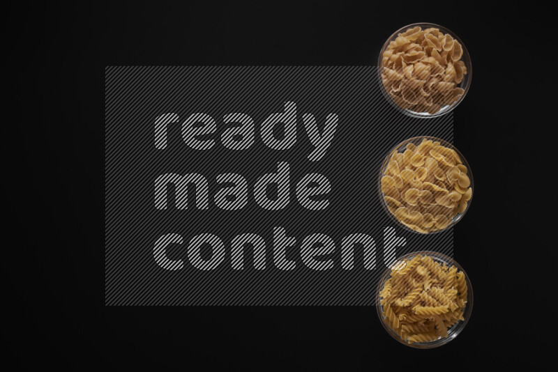 Different pasta types in 3 glass bowls on black background