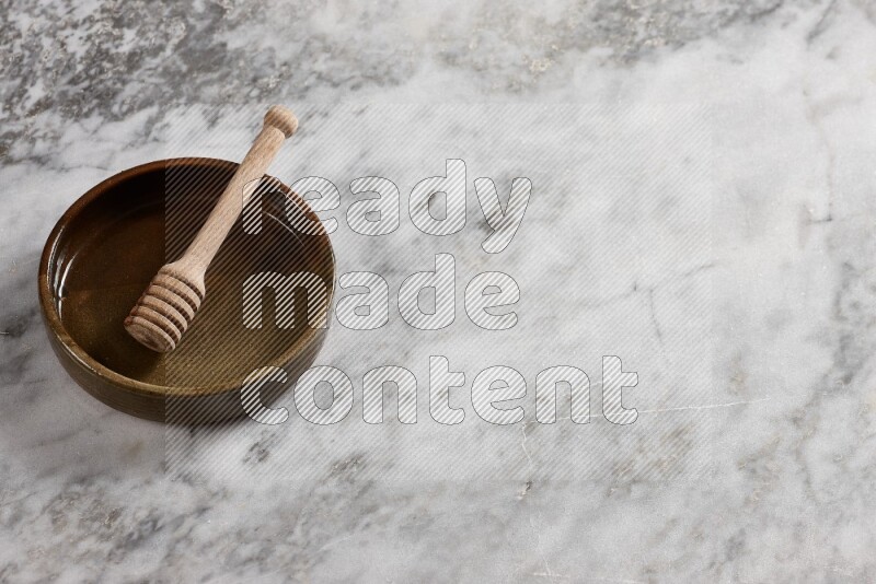 Multicolored pottery oven plate with wooden honey dipper in it on grey marble background