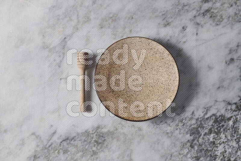Multicolored pottery plate with wooden honey dipper on the side on grey marble background