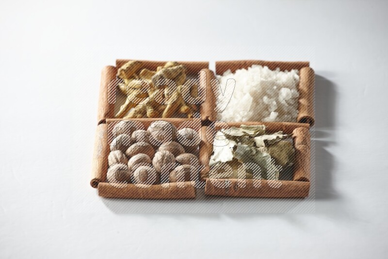 4 مربعات من أعواد القرفة ممتلئة بالملح وورق الغار وجوزة الطيب والكركم على أرضية بيضاء