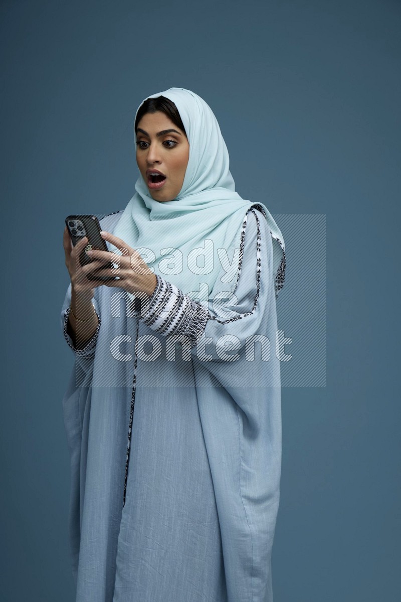 A Saudi woman Texting in a blue background wearing a blue Abaya with hijab