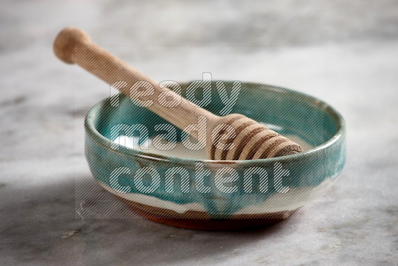 Multicolored Pottery bowl with wooden honey handle in it, on grey marble flooring, 15 degree angle