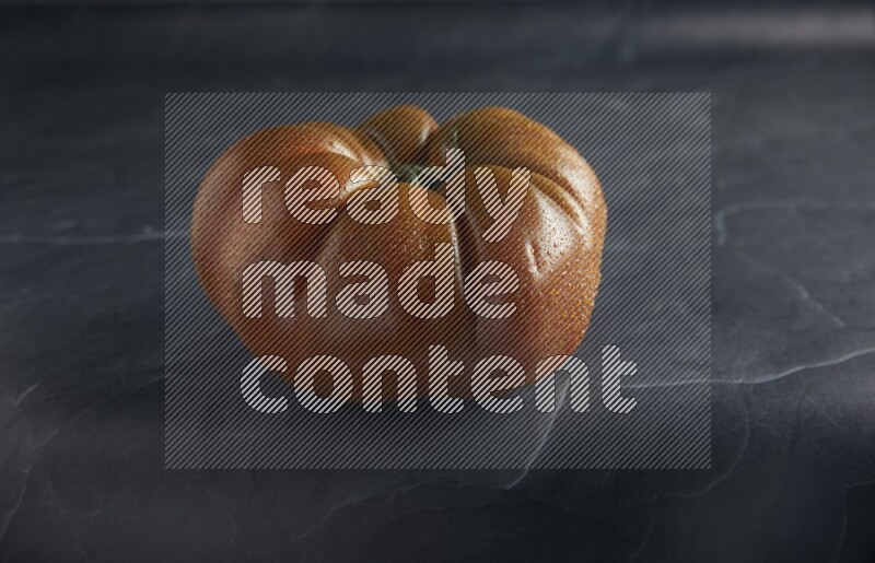 45 degree single heirloom tomato on a textured black slate background