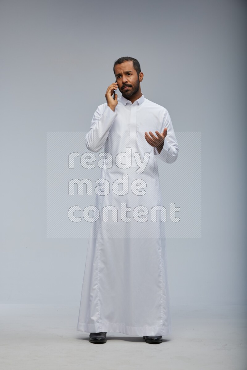 Saudi man wearing Thob standing talking on phone on Gray background