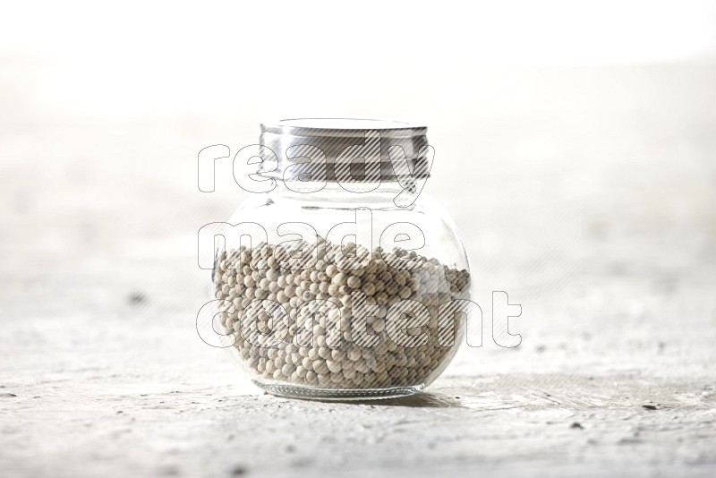 Herbal Glass jar full of white pepper beads on textured white flooring