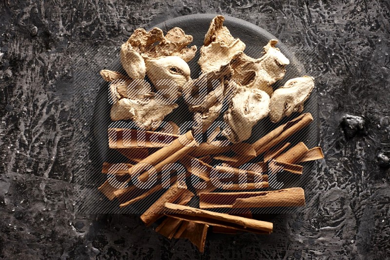 Ginger and cinnamon sticks on a black plate on textured black background