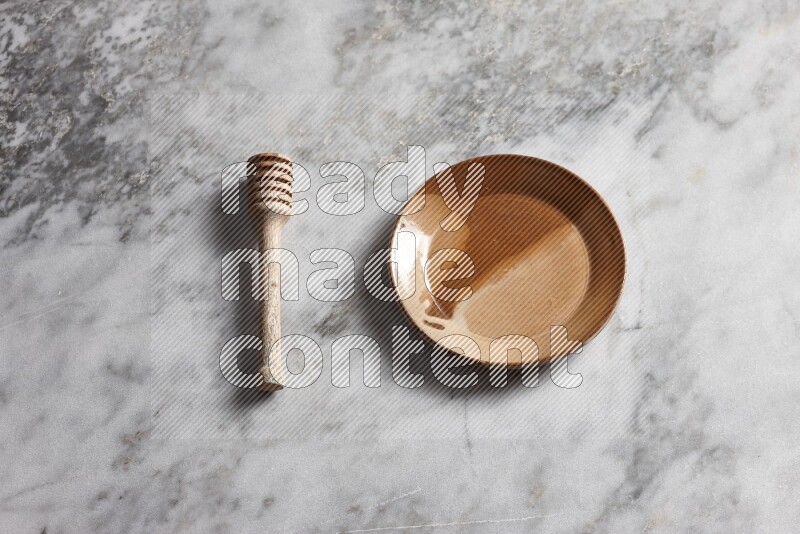 Multicolored pottery plate with wooden honey dipper on the side on grey marble background