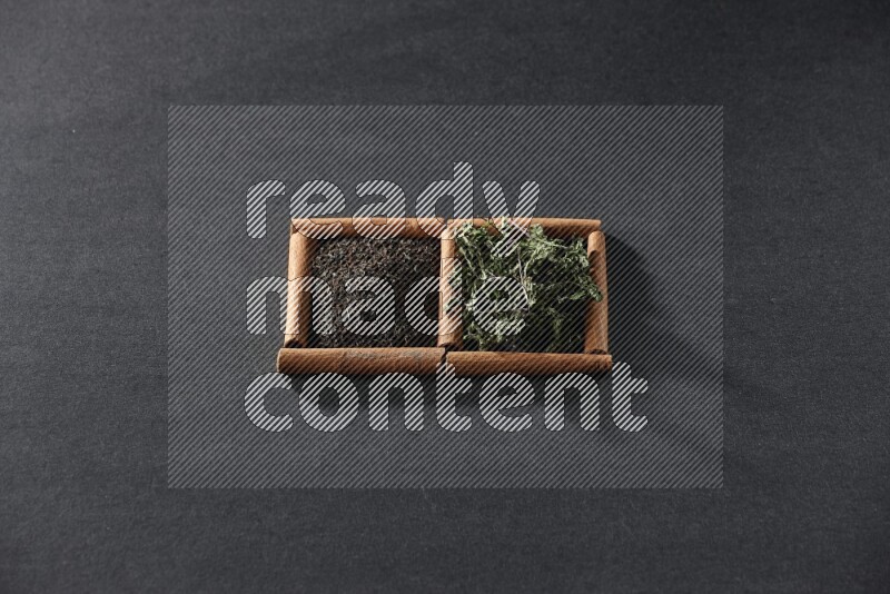 مربعان من أعواد القرفة ممتلئان بالشاي والنعناع المجفف علي خلفية سوداء