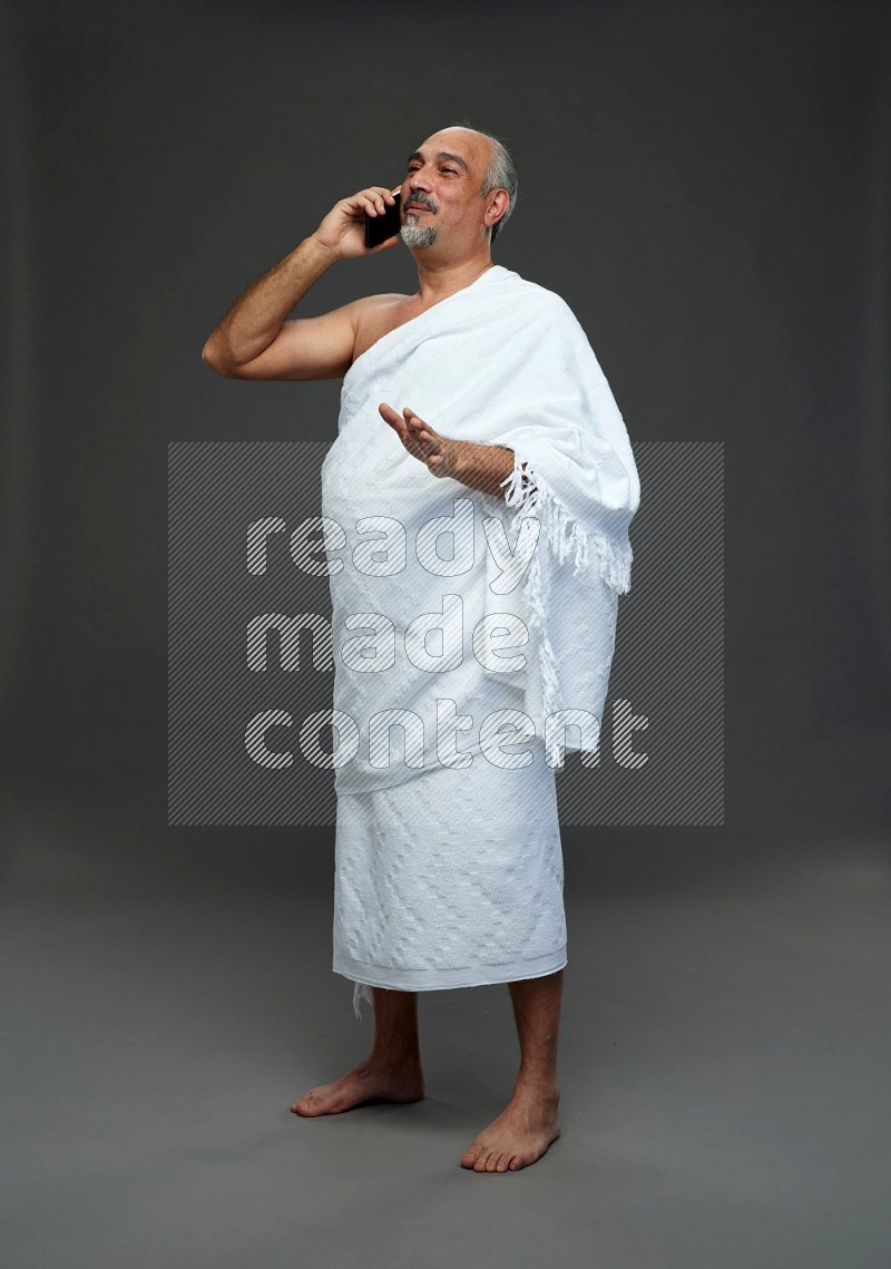 A man wearing Ehram Standing talking on phone on gray background