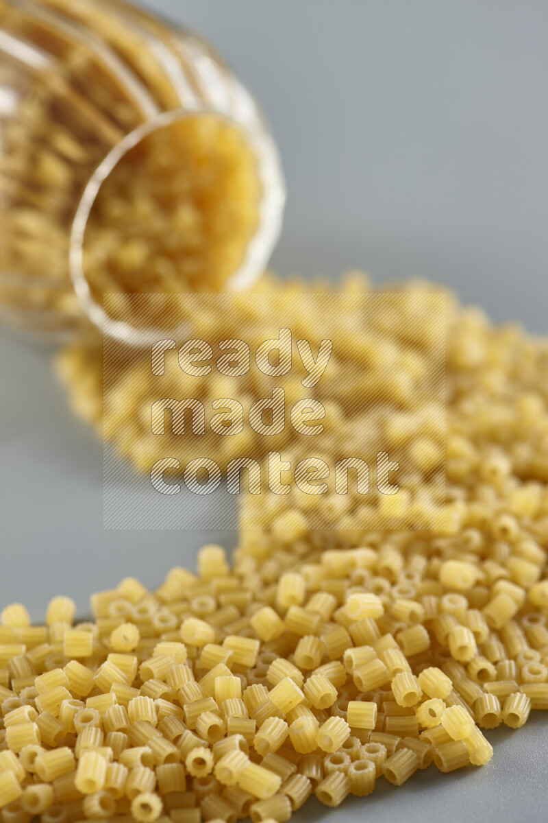 Flipped jar full of raw pasta on light blue background