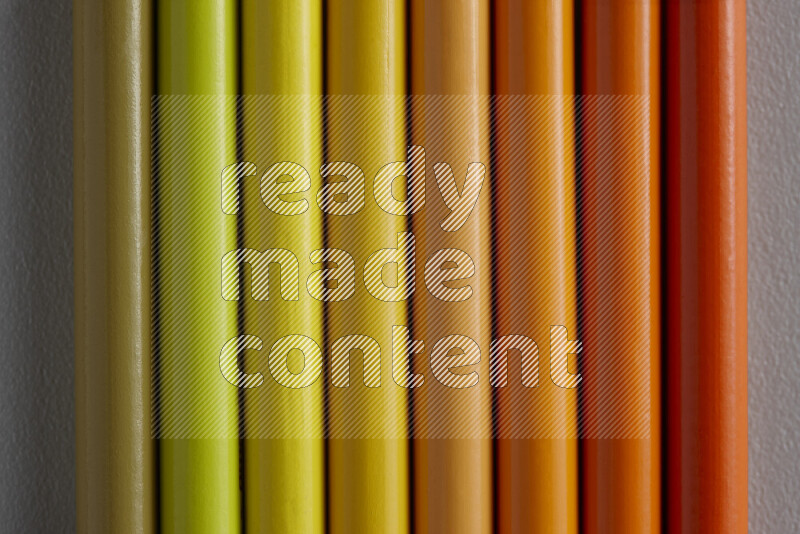 A collection of sharpened colored pencils arranged showcasing a gradient of yellow and orange hues on grey background