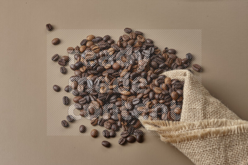 Spilled roasted coffee beans from its pack on beige background