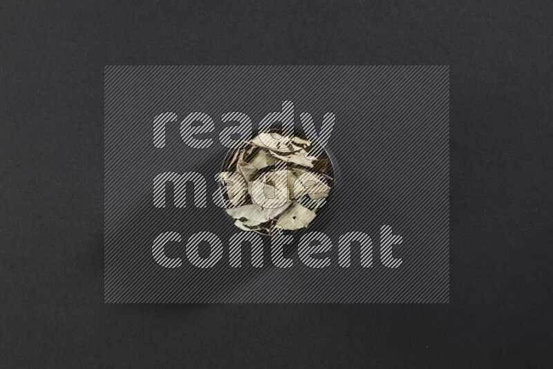 وعاء فخاري أسود ممتلئ بأوراق الغار المجففة على أرضية سوداء